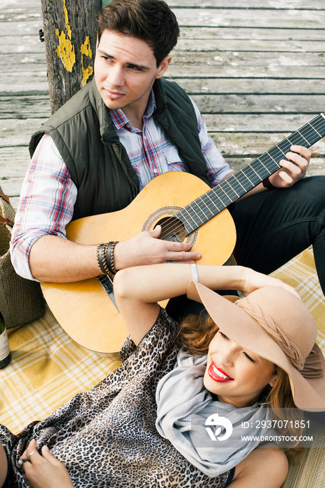 Young couple with acoustic guitar reclining on pier