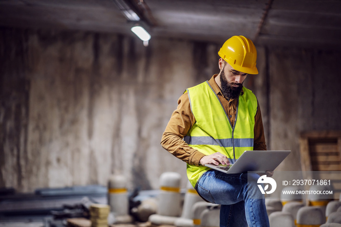 Young attractive focused bearded supervisor in vest with helmet on head standing inside of undergrou