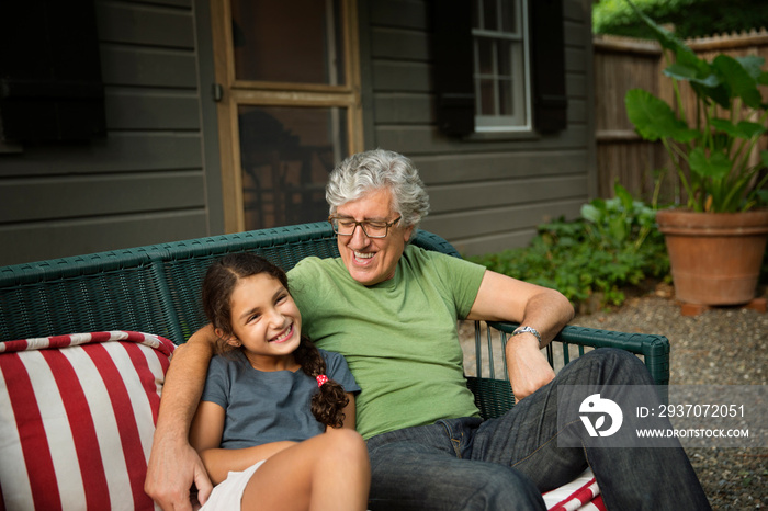 Smiling grandfather and granddaughter sitting on sofa outdoors