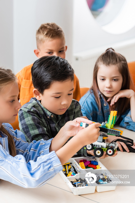 Selective focus of multiethnic kids with building blocks modeling robot in stem school