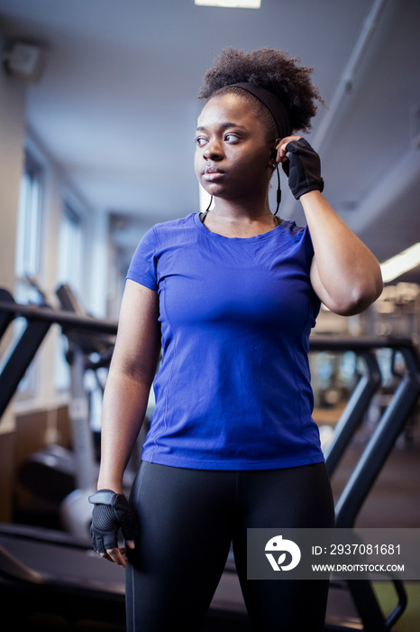 Low angle view of confident serious female athlete with headphones looking away while standing in gy