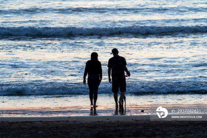 silhouette of young latin couple walking on the beach at sunset