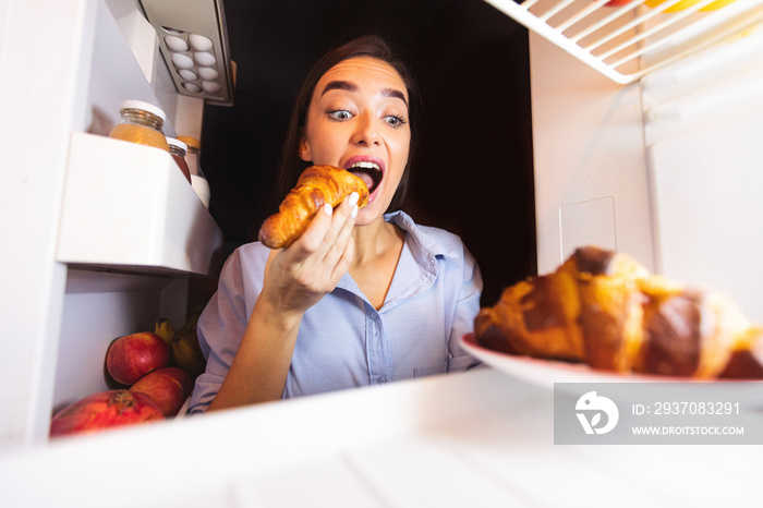 Young woman taking plate with croissants from fridge