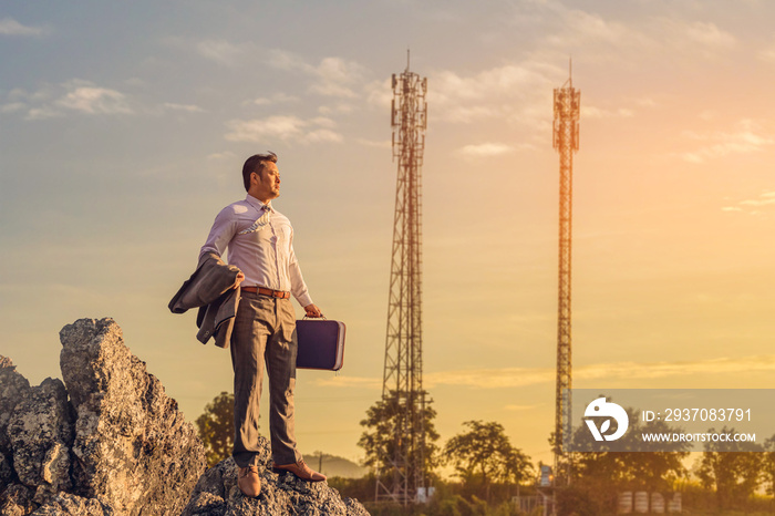 business man, holding his business attache and standing on the top of mountain looking Telecommunica