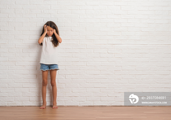 年轻的西班牙孩子因为压力而头部疼痛，手放在头上，站在白色砖墙上。