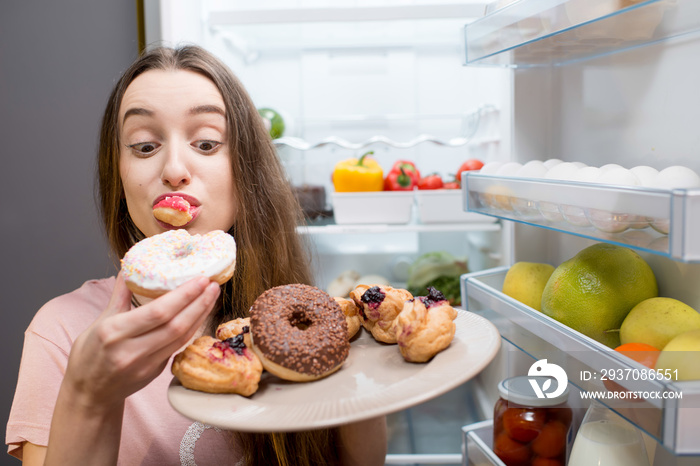 穿着睡衣的年轻女子在冰箱附近吃甜甜圈