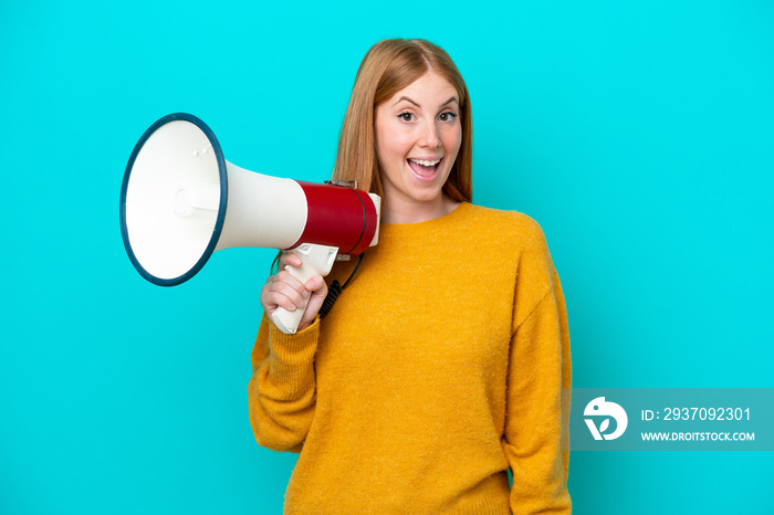 Young redhead woman isolated on blue background holding a megaphone and with surprise expression