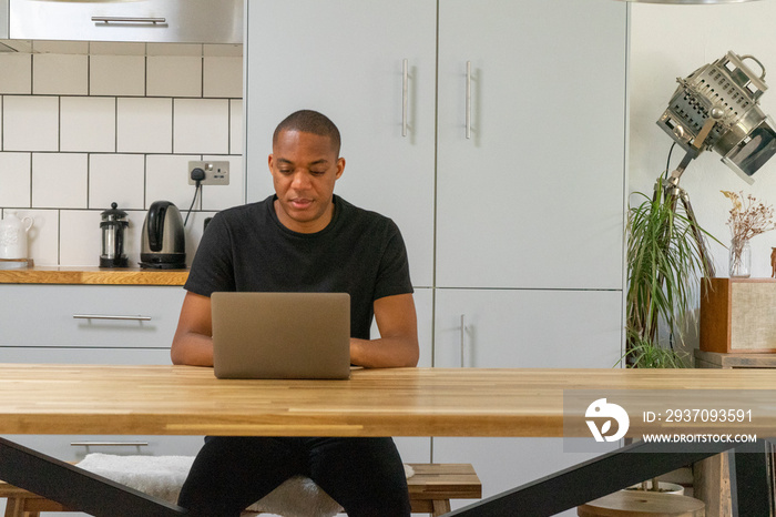 UK, London, Man using laptop at kitchen table