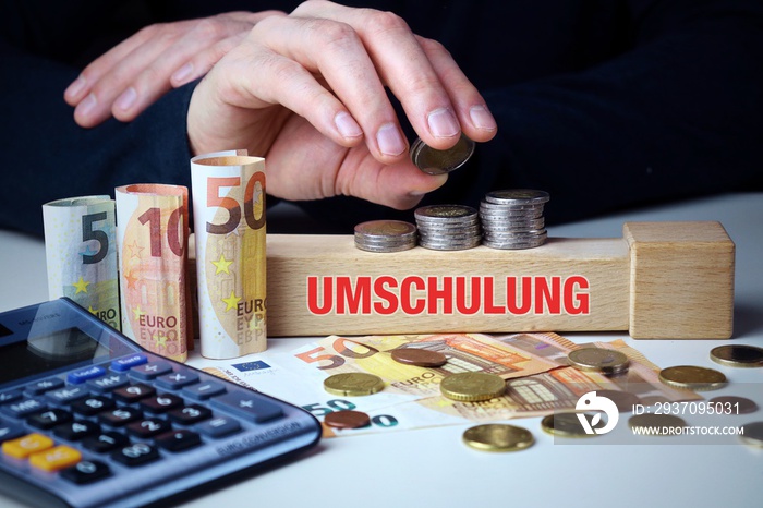 Umschulung. Männliche Hand stapelt Geld-Turm (Euro). Begriff an Baustein. Münzen, Scheine & Taschenr