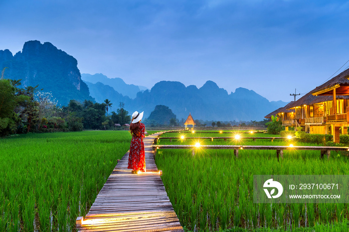 老挝万荣，一名年轻女子走在有绿色稻田的木路上。