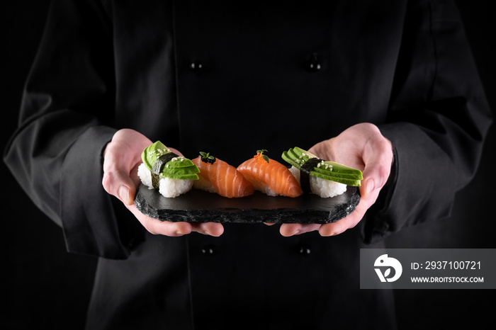 Sushi served on stone slate in chef hands on dark background. Decorated sashimi nigiri with salmon a