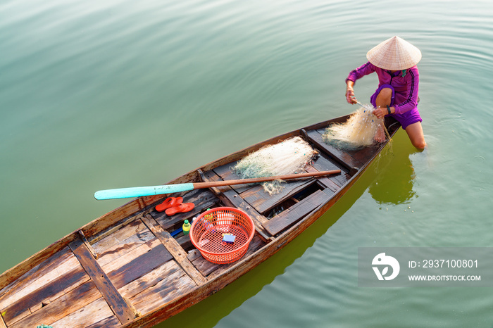 Vietnamese woman in bamboo hat checking her fishing net. Hoian