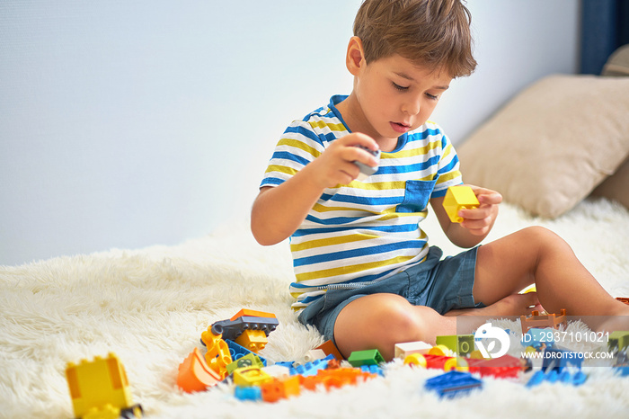 happy asian boy playing with colorful construction plastic blocks on white Bed at home.