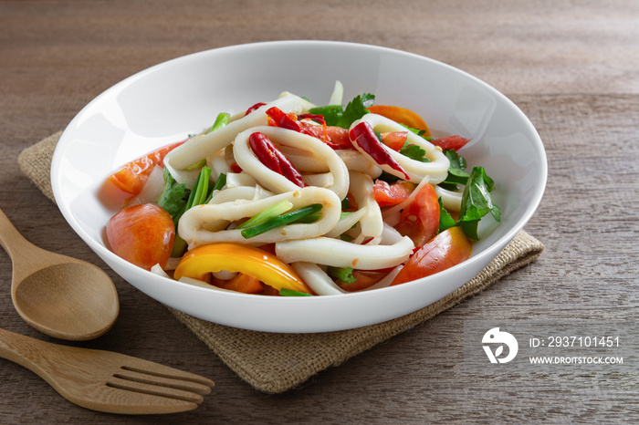 spicy squid ring salad in a ceramic plate on wooden table, close up. homemade style food concept.