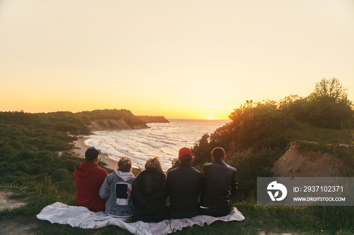 A group of friends watching the sunset at sea. View from the back. High-quality photo