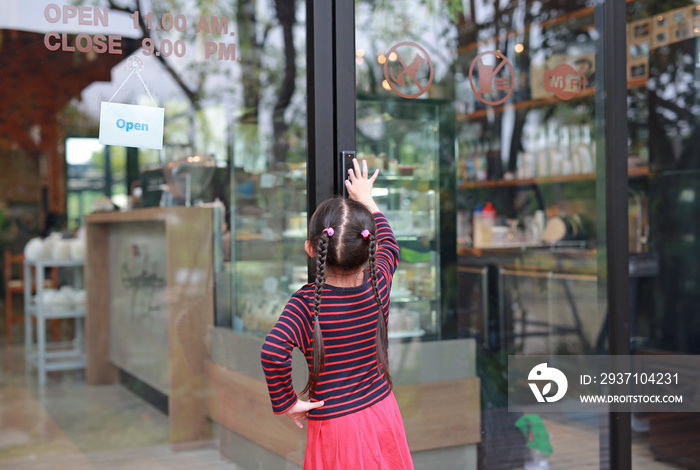 亚洲小孩按下开关打开餐厅正面玻璃门的后视图。