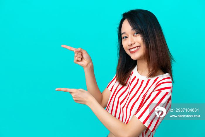 Young Vietnamese woman isolated on blue background pointing finger to the side and presenting a prod