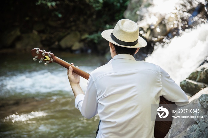 Man play ukulele new to the waterfall - people and music instrument life style in nature concept