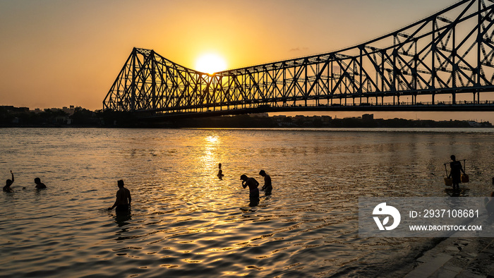 Silhouette of Howrah Bridge at the time of Sunrise.  People bathing and making rituals in the River 