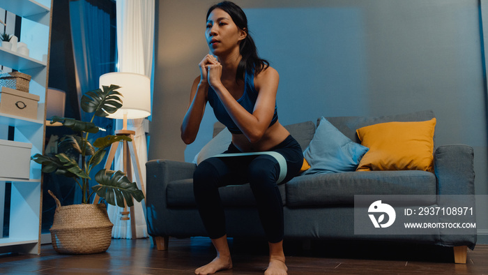 Young Asia lady in sportswear doing squat exercise working out in living room at home at night. Spor