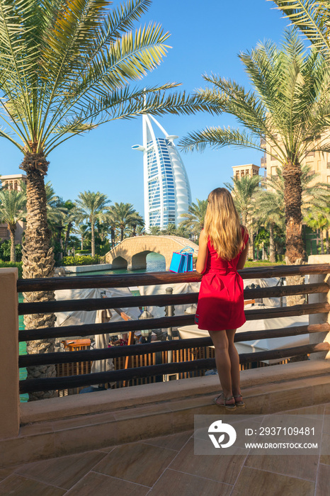 Young tourist woman dressed in red dress looking Burj al Arab from Madinat Jumeirah souk with shoppi