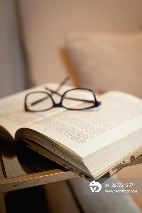 Close-up of book and glasses against blurred armchair