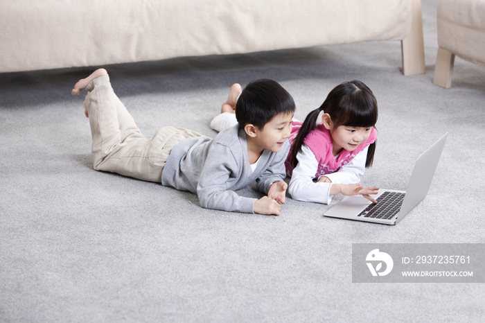 小男孩和小女孩在地毯上看笔记本电脑