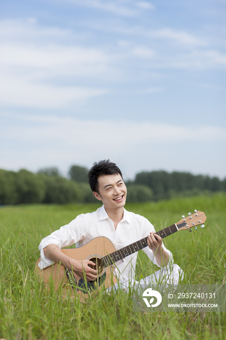 草地上的年轻男子弹奏吉他
