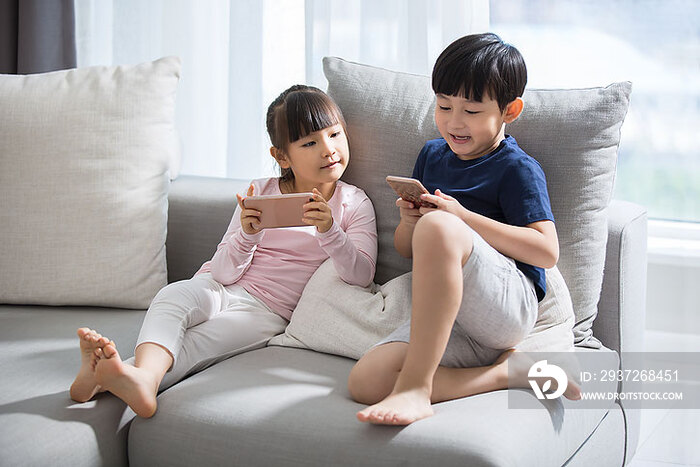 小男孩和小女孩在沙发上玩手机