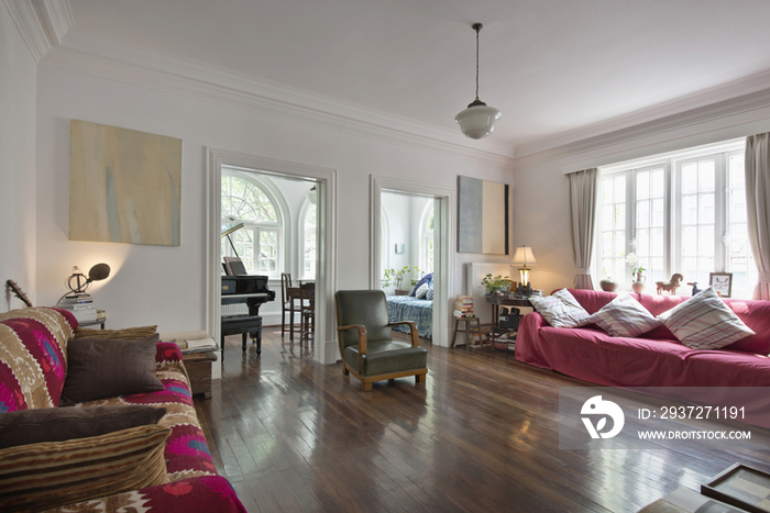 Spacious living room with wooden floor and piano in the neighboring room at home