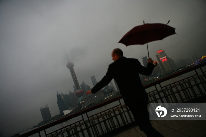 阴雨天外滩黄浦江边一位外国商务人士拿伞跳跃