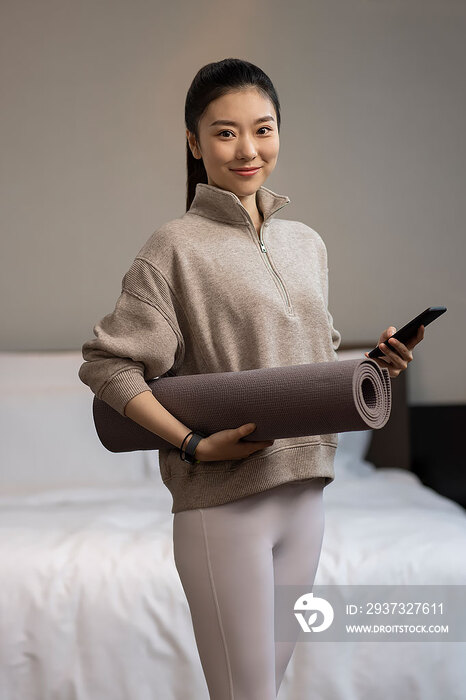 年轻女子拿着瑜伽垫和手机