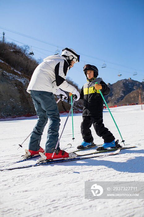 小男孩跟着教练在户外学滑雪