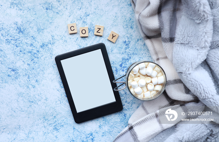 Winter and Christmas themed top view of an ebook, marshmallow hot chocolate, and a cozy soft blanket