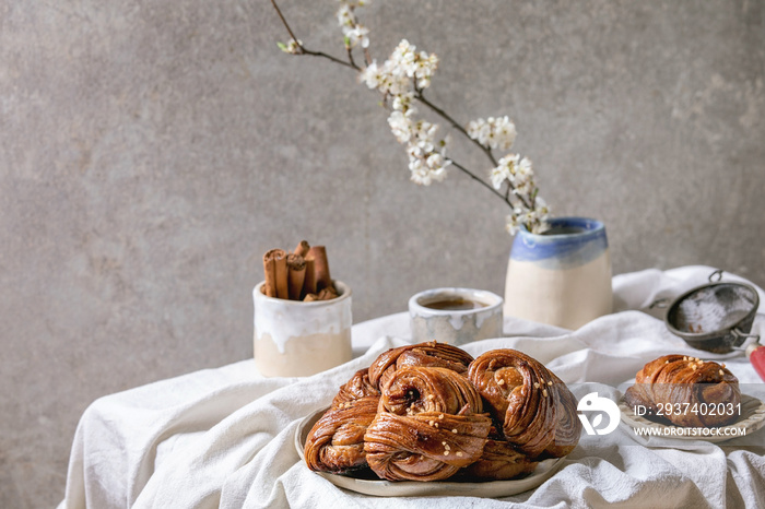 Traditional Swedish cinnamon sweet buns Kanelbulle on ceramic plate, jug of syrup, blossom branches 