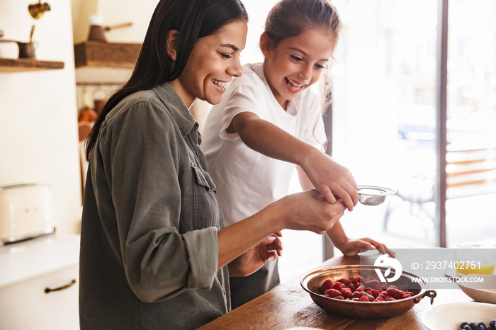 积极的家庭妇女和她的小女儿在舒适的环境中一起用覆盆子做饭的画面