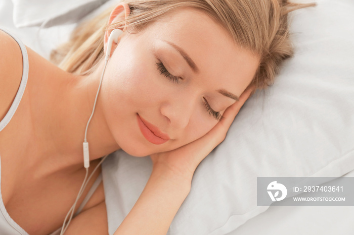 美丽的年轻女子在家里躺在床上听音乐