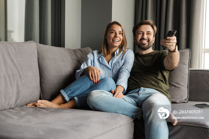 Photo of joyful couple watching TV and using remote control