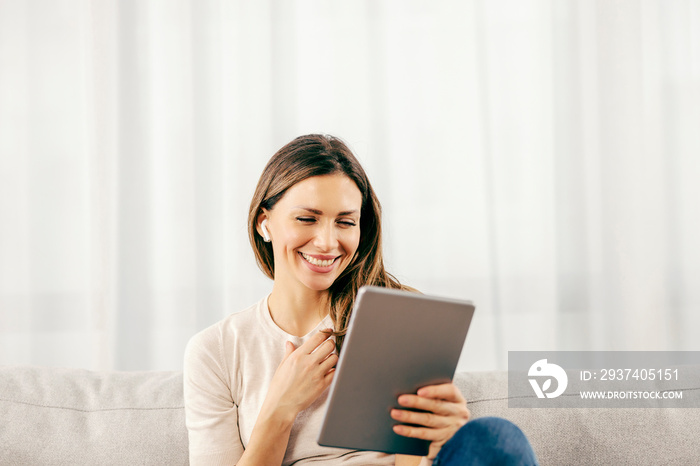 一个快乐的女人坐在沙发上，在家里的平板电脑上进行视频通话。