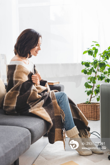 beautiful happy girl with blanket warming up with heater in cold room