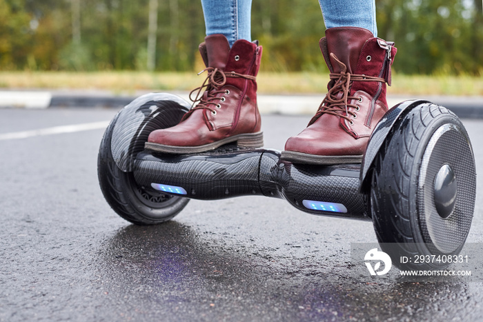 Close up of woman using hoverboard on asphalt road. Feet on electrical scooter outdoor