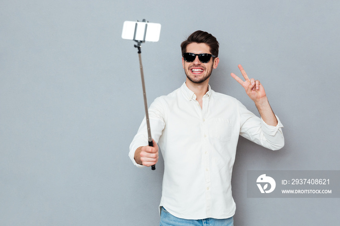 Man wearing sunglasses taking photos with smartphone and selfie stick