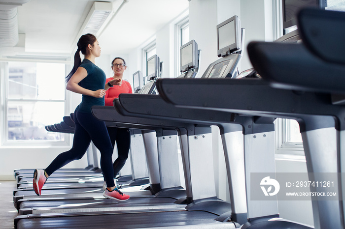 Female athletes talking while exercising on treadmills in gym