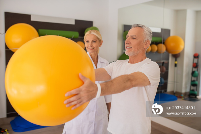 A female physical therapist in lab coat working with patient with a ball