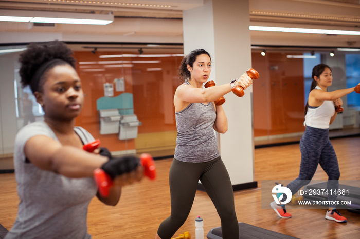 Female athletes exercising with dumbbells while standing on hardwood floor in gym