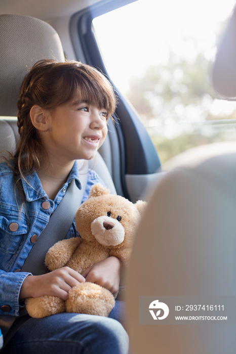 Smiling girl with teddy bear riding in backseat of car