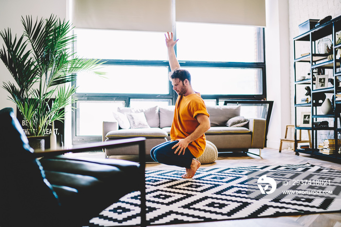 Young man sitting on tiptoes and practicing yoga pose in modern living room