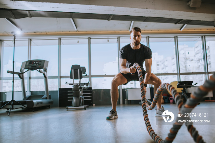 Young man practicing with battle ropes in the gym