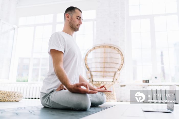 Calm caucasian man with closed eyes sitting in lotus pose meditating feeling mindfulness and spiritu