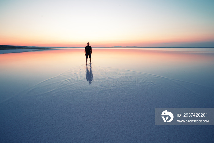 Silhouette of man departing into sunset on smooth water of lake